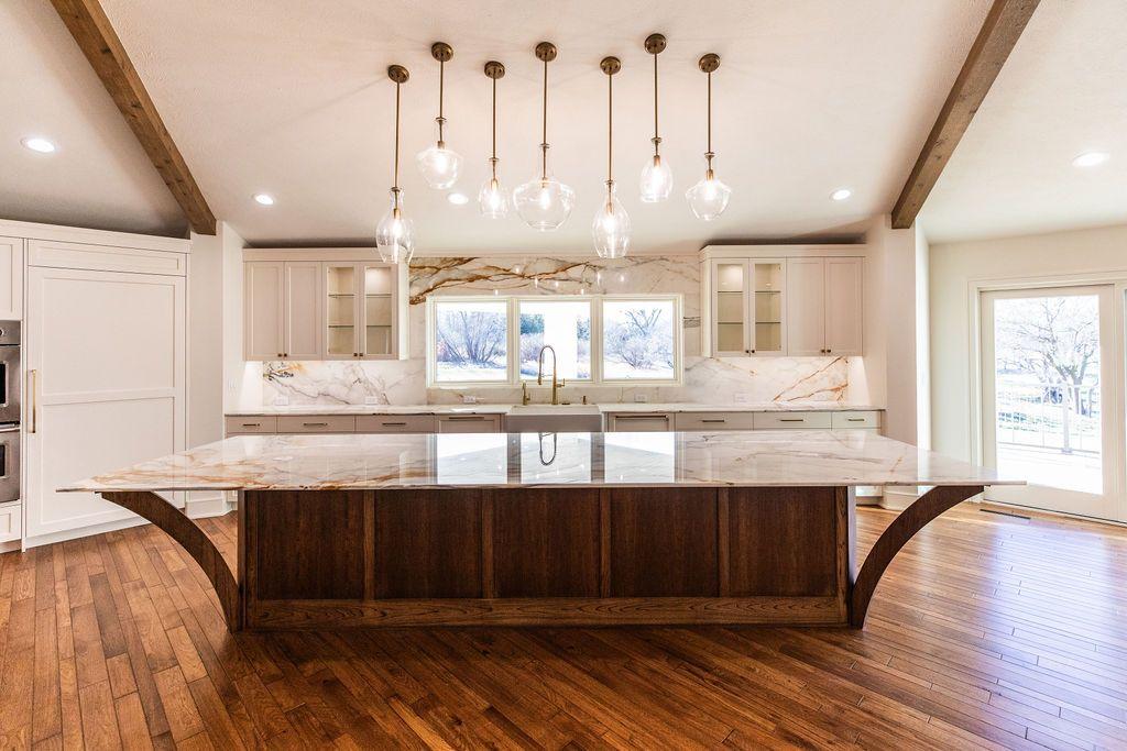Modern kitchen with large marble island, pendant lights, wooden floors, and white cabinetry.