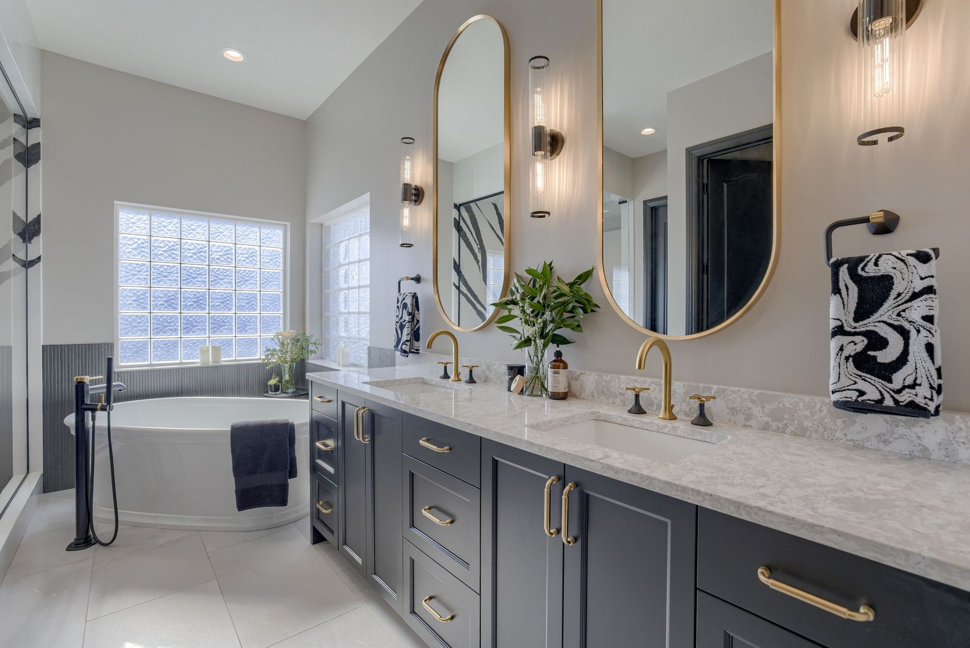 Modern bathroom with dual sink vanity, round mirrors, and large bathtub under glass block window.