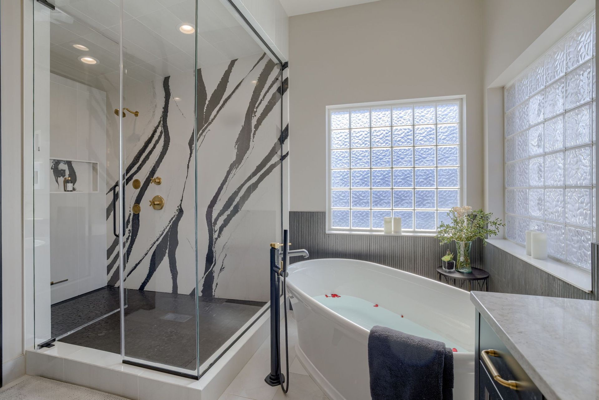 Modern bathroom with glass shower, freestanding tub, and natural light from frosted windows.